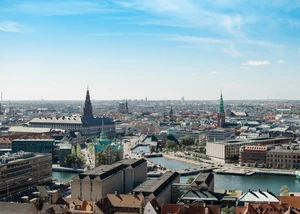 Panoramablick auf eine europäische Stadt mit markanten Kirchtürmen und einem beeindruckenden historischen Gebäude, umgeben von modernen Gebäuden und urbaner Landschaft.