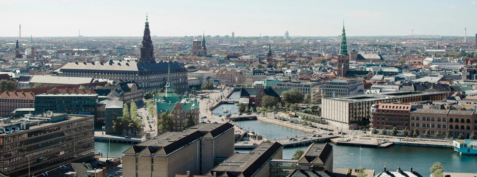 Panoramablick auf eine europäische Stadt mit markanten Kirchtürmen und einem beeindruckenden historischen Gebäude, umgeben von modernen Gebäuden und urbaner Landschaft.