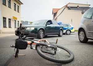 Ein Fahrrad liegt nach einem Verkehrsunfall auf der Straße mit Polizeieinsatz. Umgestürztes Fahrrad auf Straße nach Verkehrsunfall mit Polizeiauto im Hintergrund.