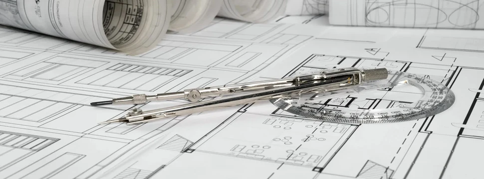 Architekturpläne und Zeichenwerkzeuge auf einem Arbeitstisch. Technische Bauzeichnungen mit Zirkel und Geodreieck, dahinter aufgerollte Architekturpläne auf weißem Papier.