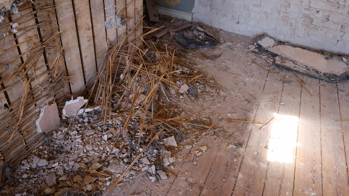 Galerie-Bild 3: Eine Baustelle in einem Altbau mit Bauschutt auf dem Holzboden und einer teilweise abgerissenen Wand, die die Lehmwickel zeigt.