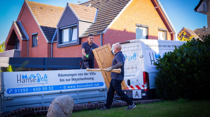 Galerie-Bild 1: Zwei Arbeiter der Firma Hanse-Belt verladen bei einer Haushaltsauflösung eine Holztür auf einen Anhänger vor einem Wohnhaus.