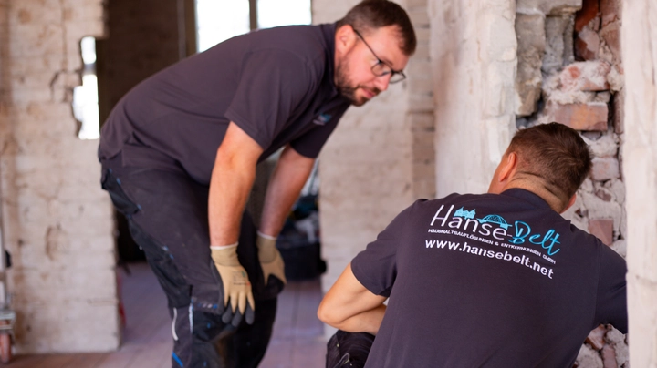 Galerie-Bild 1: Zwei Handwerker in Arbeitskleidung begutachten eine freigelegte Ziegelwand auf einer Baustelle in einem Altbau.