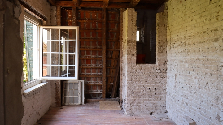 Galerie-Bild 4: Ein heller Raum im Rohbau eines Altbaus während der Sanierung mit freigelegten Backsteinwänden, Holzboden und offenem Fenster.
